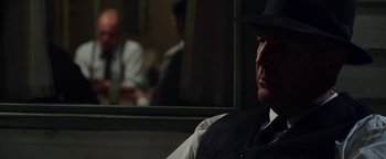 Movie still from “The Highwaymen” (2019), directed by John Lee Hancock – A man wearing a hat and a vest sitting in front of a window; Close Up shot, Over the shoulder angle