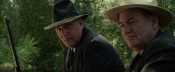 Movie still from “The Highwaymen” (2019), directed by John Lee Hancock – A man wearing a suit and a hat is sitting next to another man wearing a hat; Close Up shot, Over the shoulder angle