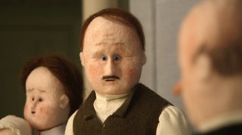Movie still from “The House” (2022), directed by Paloma Baeza – A doll's head with a man's face in the background; Close Up shot, Over the shoulder angle