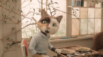 Movie still from “The House” (2022), directed by Paloma Baeza – A cat wearing a shirt is sitting at a table with food; Medium shot, High angle