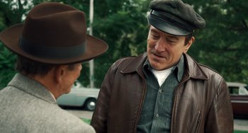 Movie still from “The Irishman” (2019), directed by Martin Scorsese – A man wearing a hat and a leather jacket talking to another man; Medium shot, Over the shoulder angle