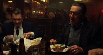 Movie still from “The Irishman” (2019), directed by Martin Scorsese – Two men sitting at a table with plates of food in front of them; Medium shot, Over the shoulder angle