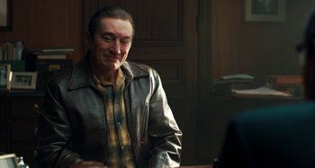 Movie still from “The Irishman” (2019), directed by Martin Scorsese – An older man wearing a leather jacket sitting at a table; Medium shot, Over the shoulder angle