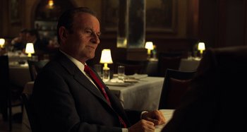 Movie still from “The Irishman” (2019), directed by Martin Scorsese – An older man in a suit and red neck tie sitting in front of a computer; Medium shot, Over the shoulder angle