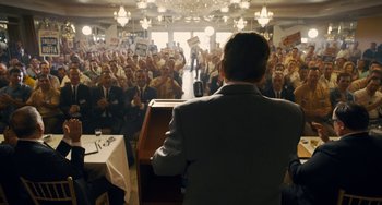 Movie still from “The Irishman” (2019), directed by Martin Scorsese – A crowd of people in a room with a man standing at a podium; Wide shot, High angle
