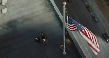 Movie still from “The Irishman” (2019), directed by Martin Scorsese – An aerial view of people walking on a sidewalk near an american flag; Extreme Wide shot, Overhead angle