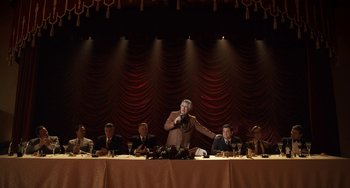 Movie still from “The Irishman” (2019), directed by Martin Scorsese – A man standing in front of a microphone in front of a group of people; Wide shot, Low angle