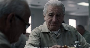 Movie still from “The Irishman” (2019), directed by Martin Scorsese – An older man sitting at a table eating a hot dog; Close Up shot, Over the shoulder angle
