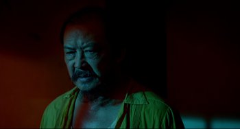 Movie still from “Only God Forgives” (2013), directed by Nicolas Winding Refn – An older man with a beard and mustache wearing a green shirt; Close Up shot, Low angle