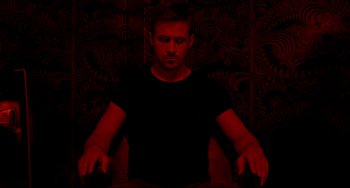Movie still from “Only God Forgives” (2013), directed by Nicolas Winding Refn – A man in a black shirt is sitting in a chair; Medium shot, Overhead angle
