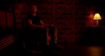 Movie still from “Only God Forgives” (2013), directed by Nicolas Winding Refn – A man sitting in a chair in a room with red walls; Wide shot, High angle