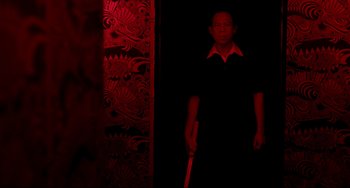 Movie still from “Only God Forgives” (2013), directed by Nicolas Winding Refn – A man standing in a dark room holding a sword; Medium shot, Over the shoulder angle