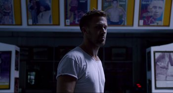 Movie still from “Only God Forgives” (2013), directed by Nicolas Winding Refn – A man standing in front of a wall with pictures on the wall behind him; Medium shot, Over the shoulder angle