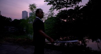 Movie still from “Only God Forgives” (2013), directed by Nicolas Winding Refn – A man holding a sword while standing in a park; Medium shot, Low angle