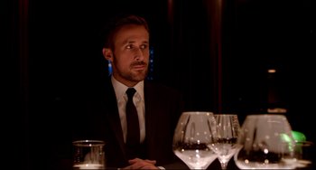 Movie still from “Only God Forgives” (2013), directed by Nicolas Winding Refn – A man sitting at a table with a glass of wine; Medium shot, Over the shoulder angle