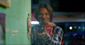 Movie still from “Only God Forgives” (2013), directed by Nicolas Winding Refn – A man holding a gun while standing next to a wall; Medium shot, Low angle