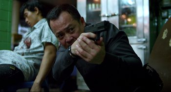 Movie still from “Only God Forgives” (2013), directed by Nicolas Winding Refn – A man holding a gun in his hand; Medium shot, Over the shoulder angle