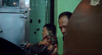 Movie still from “Only God Forgives” (2013), directed by Nicolas Winding Refn – A man holding a gun while another man is in a bathroom; Medium shot, Over the shoulder angle