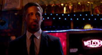 Movie still from “Only God Forgives” (2013), directed by Nicolas Winding Refn – A man wearing a suit and tie standing in front of lights; Close Up shot, Over the shoulder angle