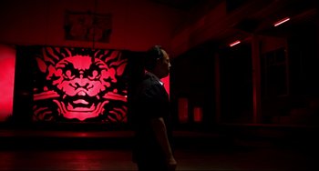 Movie still from “Only God Forgives” (2013), directed by Nicolas Winding Refn – A man standing in front of a wall with a painting on it; Wide shot, Low angle