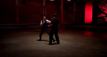 Movie still from “Only God Forgives” (2013), directed by Nicolas Winding Refn – Two men in a dark room , one of whom is holding a microphone; Wide shot, Over the shoulder angle