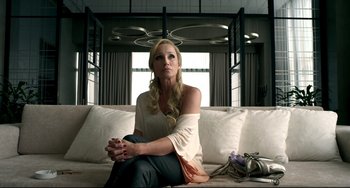 Movie still from “Only God Forgives” (2013), directed by Nicolas Winding Refn – A woman sitting on top of a couch in a living room; Medium shot, Over the shoulder angle