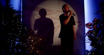Movie still from “Only God Forgives” (2013), directed by Nicolas Winding Refn – A man singing into a microphone in front of a projector; Medium shot, Low angle