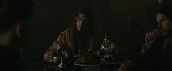 Movie still from “The King” (2019), directed by David Michôd – A man sitting at a table with a plate of food in front of him; Medium shot, Over the shoulder angle