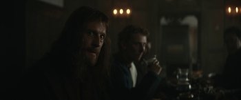 Movie still from “The King” (2019), directed by David Michôd – A man with long hair and a long beard is holding a glass of wine; Medium shot, Over the shoulder angle