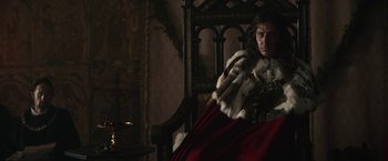 Movie still from “The King” (2019), directed by David Michôd – A man sitting in a chair wearing a robe; Medium shot, Over the shoulder angle