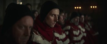 Movie still from “The King” (2019), directed by David Michôd – A group of people in red robes and chains; Close Up shot, Over the shoulder angle