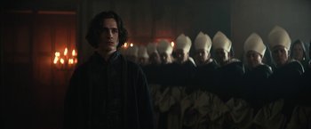 Movie still from “The King” (2019), directed by David Michôd – A group of people in a dark room with a man in a black jacket; Medium shot, Low angle