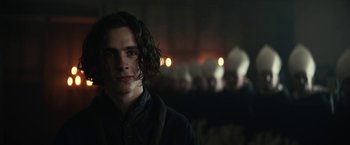 Movie still from “The King” (2019), directed by David Michôd – A man with long dark hair standing in front of a group of people; Close Up shot, Over the shoulder angle