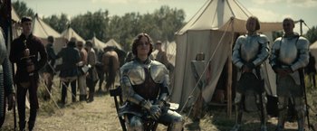 Movie still from “The King” (2019), directed by David Michôd – A man sitting in a chair wearing a suit of armor; Medium shot, Over the shoulder angle