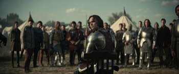Movie still from “The King” (2019), directed by David Michôd – A man in a suit of armor sitting in a chair in front of a group of people; Medium shot, Over the shoulder angle