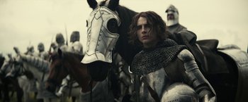 Movie still from “The King” (2019), directed by David Michôd – A man standing next to a horse in a field; Medium shot, Low angle