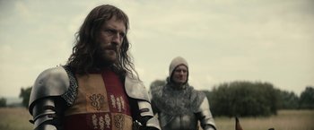 Movie still from “The King” (2019), directed by David Michôd – Two men dressed in medieval clothing standing next to each other in a field; Medium shot, Over the shoulder angle