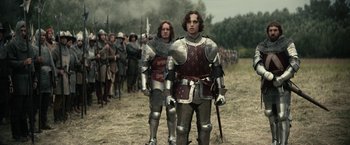 Movie still from “The King” (2019), directed by David Michôd – Two men in medieval armor standing in a field; Medium shot, Low angle