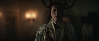 Movie still from “The King” (2019), directed by David Michôd – An older man wearing a priest's outfit in a dark room; Close Up shot, Low angle