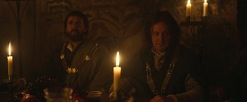 Movie still from “The King” (2019), directed by David Michôd – Two men sitting next to each other in front of a lit candle; Medium shot, Over the shoulder angle