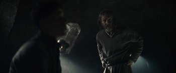 Movie still from “The King” (2019), directed by David Michôd – A man standing next to another man in a dark room; Medium shot, Over the shoulder angle