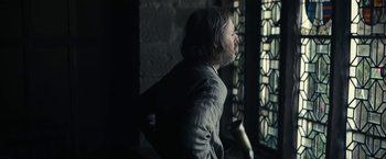 Movie still from “The King” (2019), directed by David Michôd – A man standing in front of a stained glass window; Medium shot, Over the shoulder angle