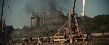 Movie still from “The King” (2019), directed by David Michôd – A group of people standing next to a wooden structure in a field; Extreme Wide shot, Low angle