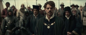 Movie still from “The King” (2019), directed by David Michôd – A man with a beard is standing in front of a crowd; Medium shot, Over the shoulder angle