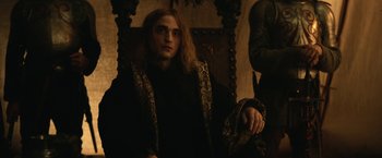 Movie still from “The King” (2019), directed by David Michôd – A man in a black robe sitting in a chair; Medium shot, Over the shoulder angle