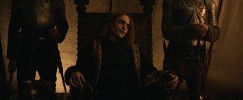 Movie still from “The King” (2019), directed by David Michôd – A man sitting in a chair in a dark room; Medium shot, High angle