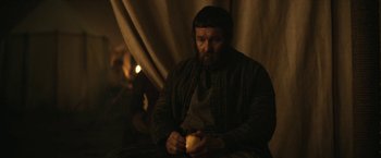 Movie still from “The King” (2019), directed by David Michôd – A man holding an apple while sitting in a chair; Medium shot, Over the shoulder angle