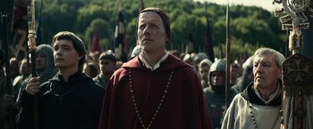 Movie still from “The King” (2019), directed by David Michôd – A man wearing a red robe and a red hat; Medium shot, Over the shoulder angle