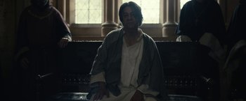 Movie still from “The King” (2019), directed by David Michôd – A man sitting on top of a couch wearing a robe; Medium shot, Low angle