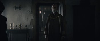 Movie still from “The King” (2019), directed by David Michôd – An old man with a long beard in a dark room; Medium shot, Over the shoulder angle
